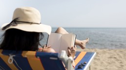 mujer leyendo un libro sobre tecnología en la playa