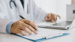 Médico rellenando un formulario médico mientras está sentado en el escritorio de la consulta del hospital