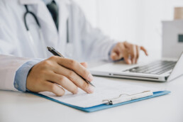 Médico rellenando un formulario médico mientras está sentado en el escritorio de la consulta del hospital